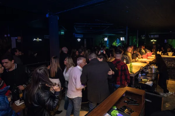 Público reunido junto ao balcão do bar, com a banda tocando ao fundo