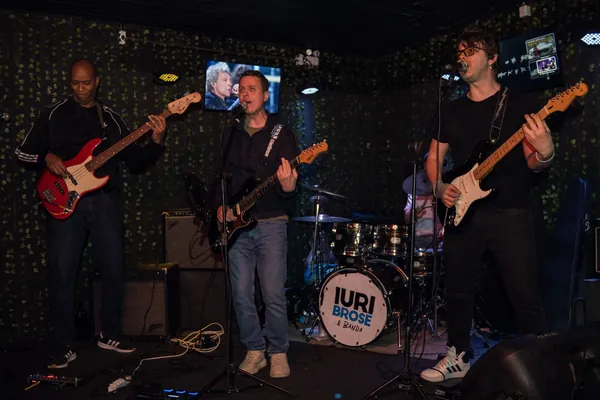 Iuri Brose e banda no palco, com o nome do grupo estampado no bumbo da bateria