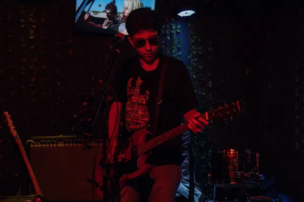 Guitarrista de óculos escuros toca sob a luz vermelha do palco