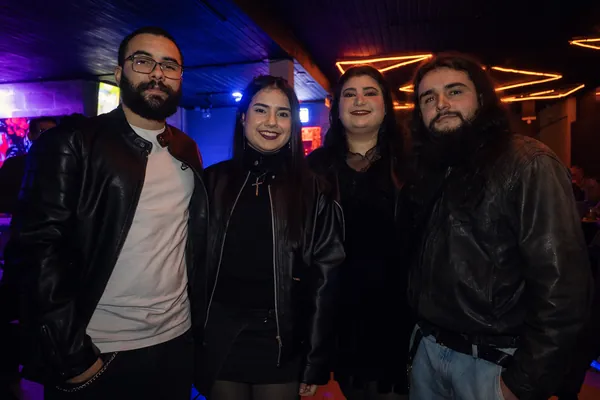 Quatro jovens de jaqueta de couro posam sob o neon laranja em ziguezague do teto