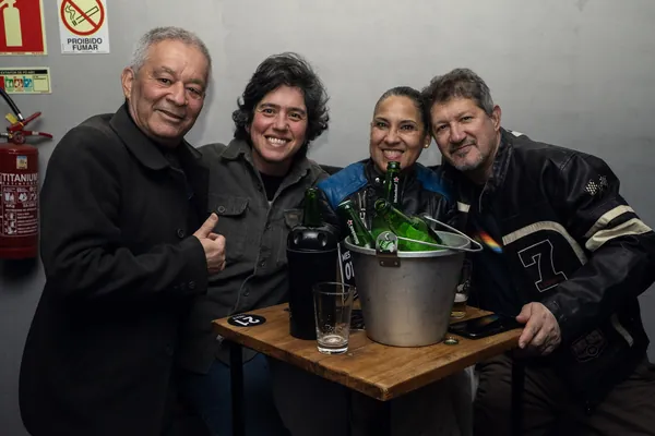 Quatro convidados posam ao redor do balde de gelo com garrafas, junto à parede de concreto