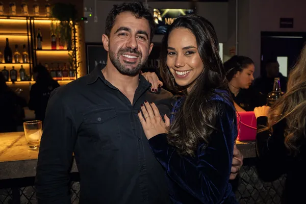 Homem e mulher posam abraçados junto ao balcão do bar