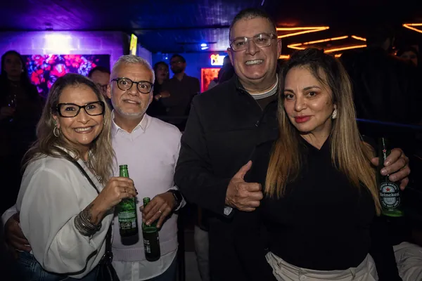 Quatro convidados posam com garrafas de cerveja, sob o neon laranja do teto