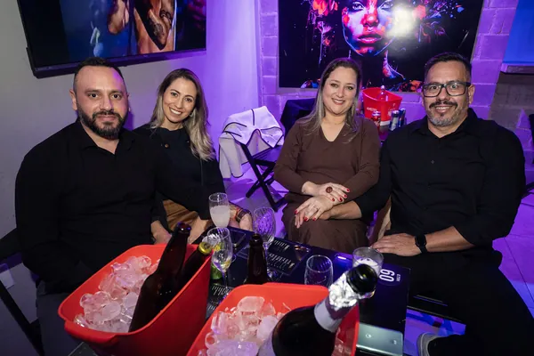 Quatro convidados sentados à mesa, com baldes de gelo vermelhos e taças sobre o tampo